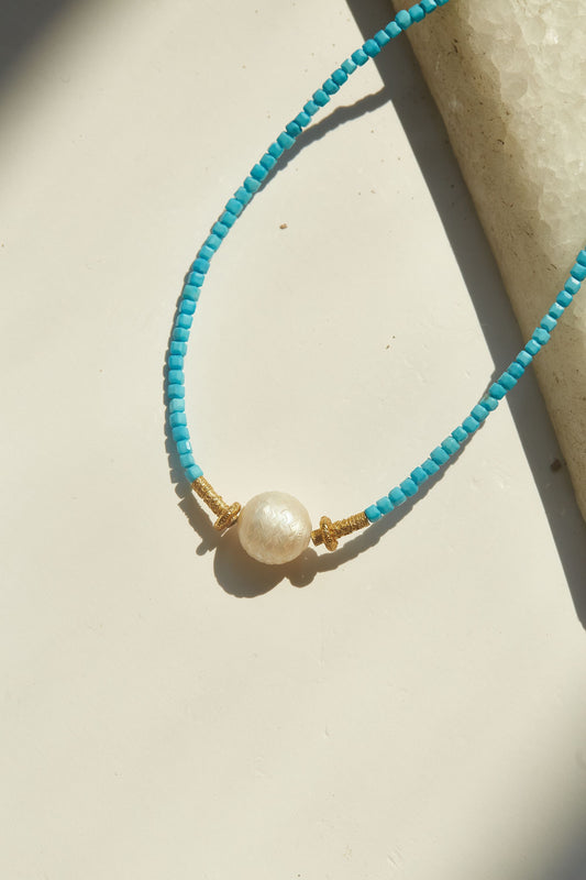 Turquoise beaded necklace with a pearl pendant on a beige surface