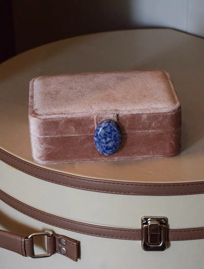 Coral pink velvet jewelry box with a blue stone on top of a beige hat box.