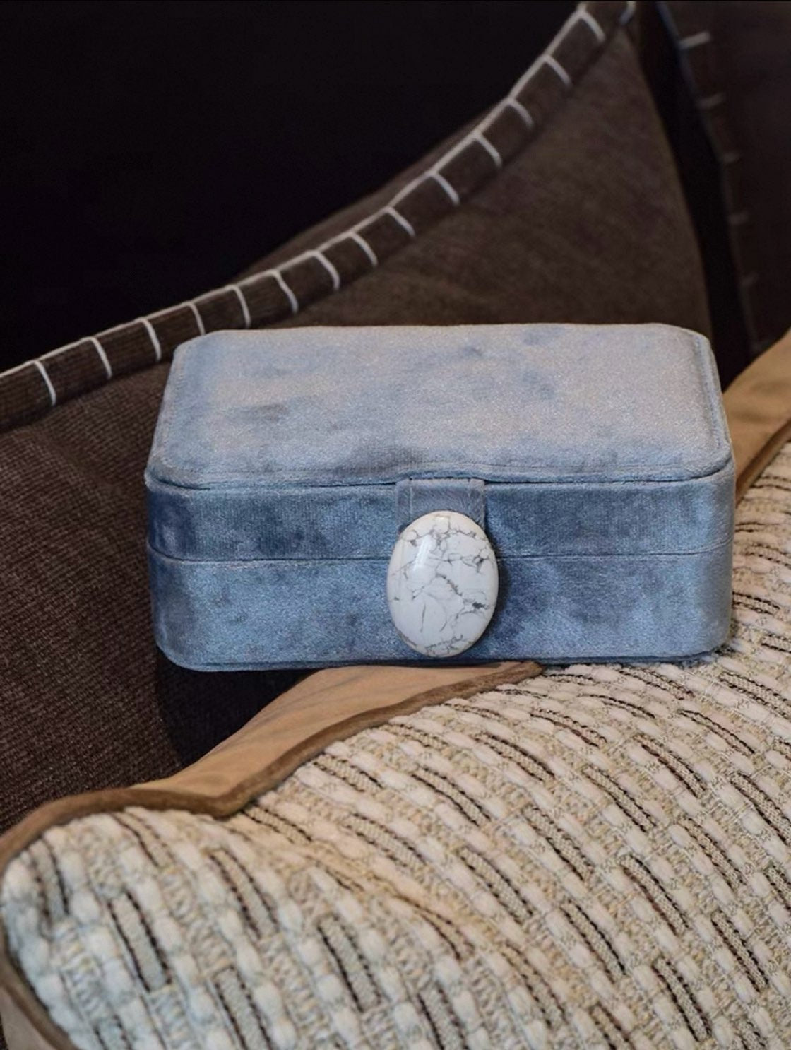 Sky blue velvet jewelry box with a stone clasp on a textured surface