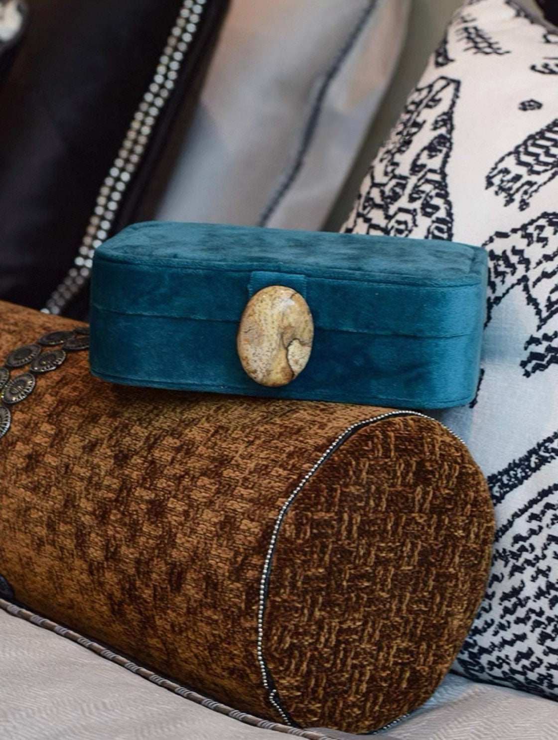 Dark cyan blue velvet jewelry box with a stone button on a textured brown pillow