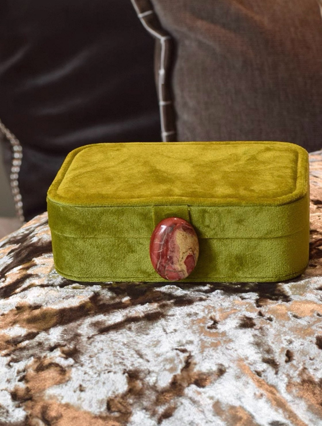 Olive green velvet jewelry box with a red stone on a textured surface