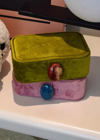 Green and pink velvet jewelry box with decorative stones on a light surface.