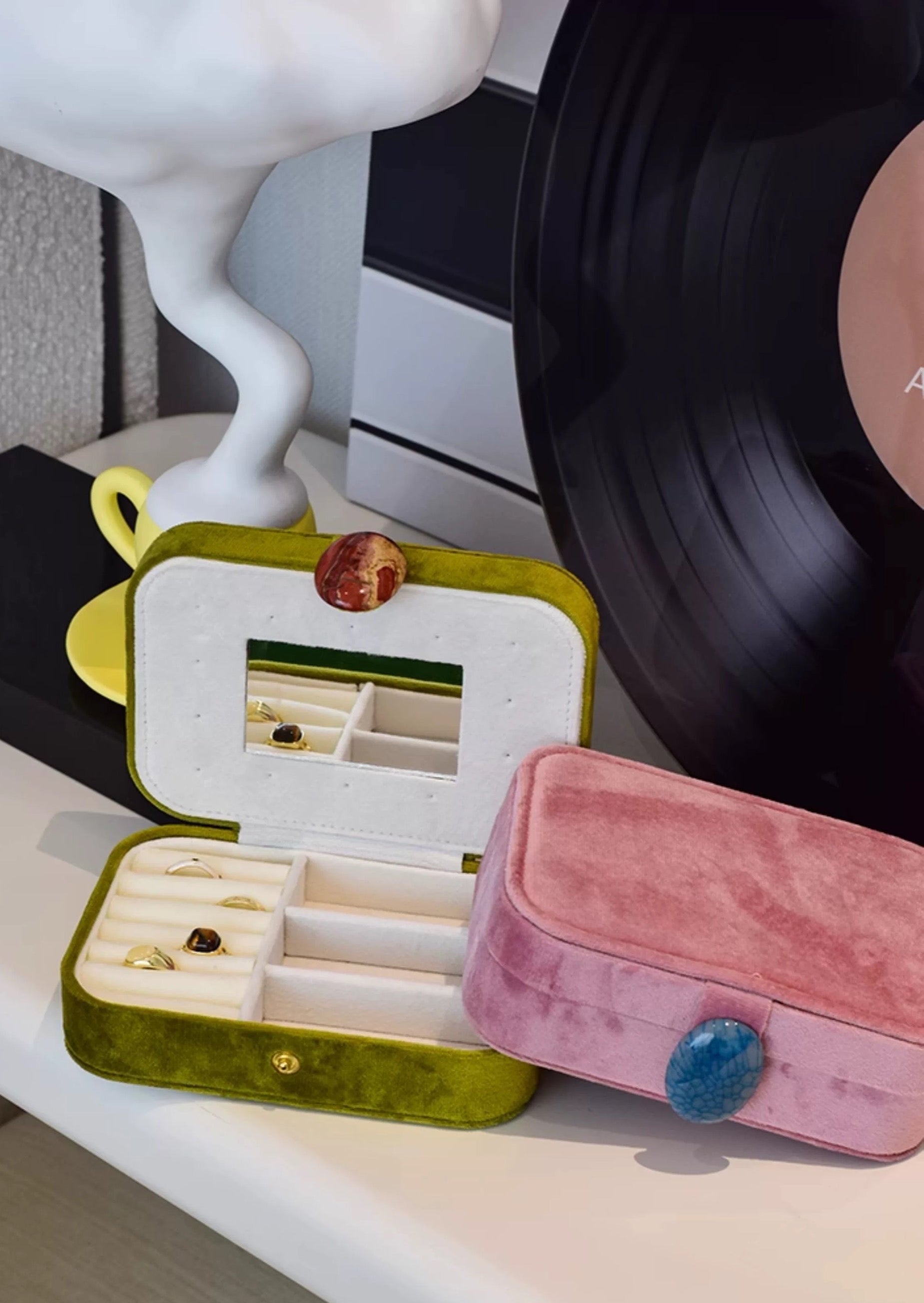 Open green jewelry box with small items on a surface next to a pink velvet box.