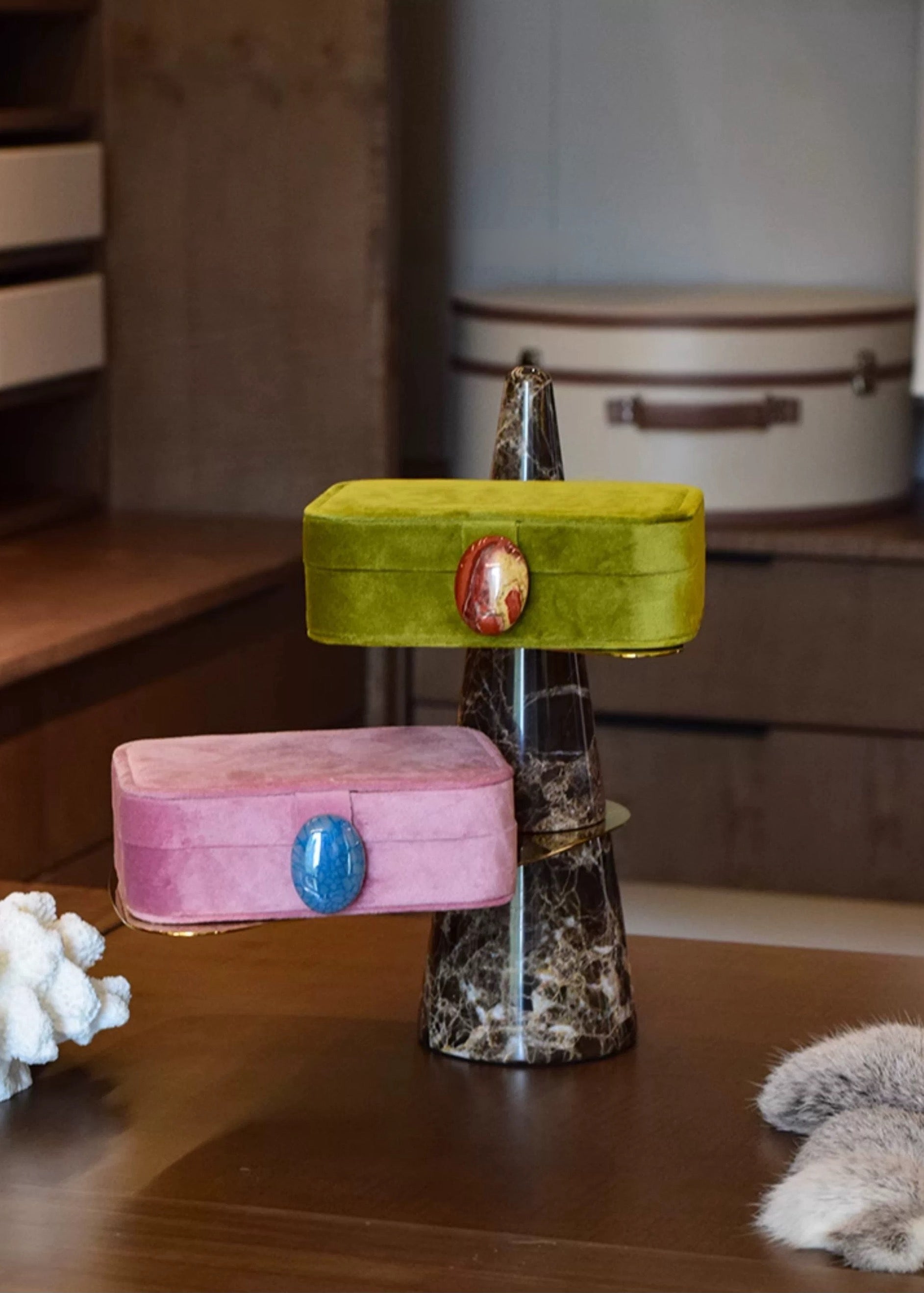 Two colorful velvet jewelry boxes on a stand with a neutral background
