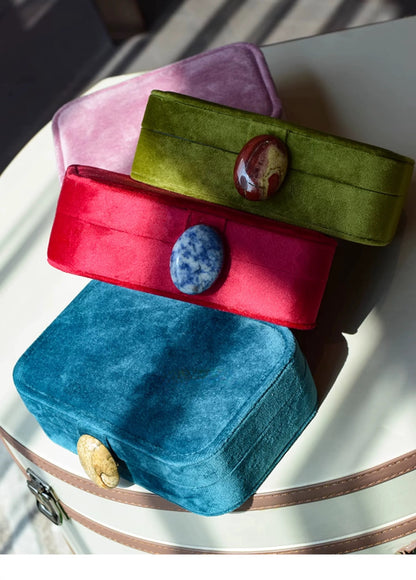 Colorful velvet jewelry boxes with stone embellishments on a white surface