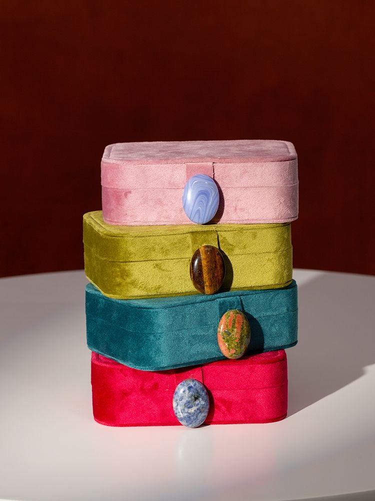 Stack of colorful velvet jewelry boxes with stone buttons on a white surface and brown background