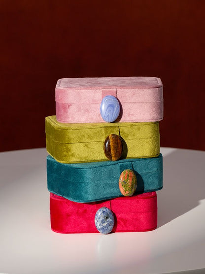 Stack of colorful velvet jewelry boxes with stone buttons on a white surface and brown background