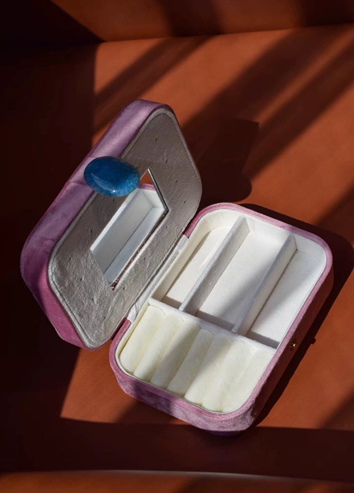 Pink jewelry box with white interior on a wooden surface
