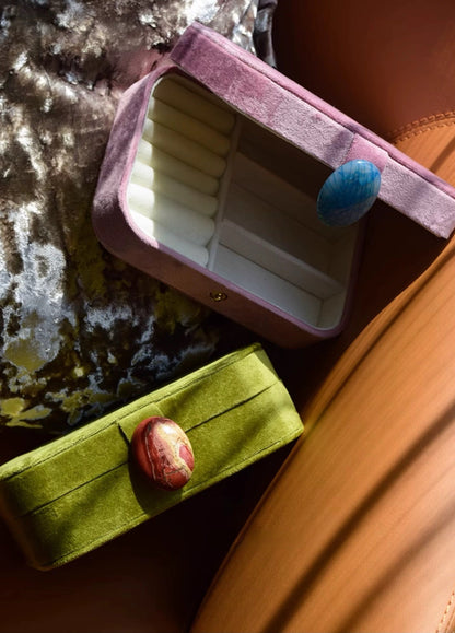 Two small velvet jewelry boxes, one purple and one green, with decorative buttons on a textured surface.
