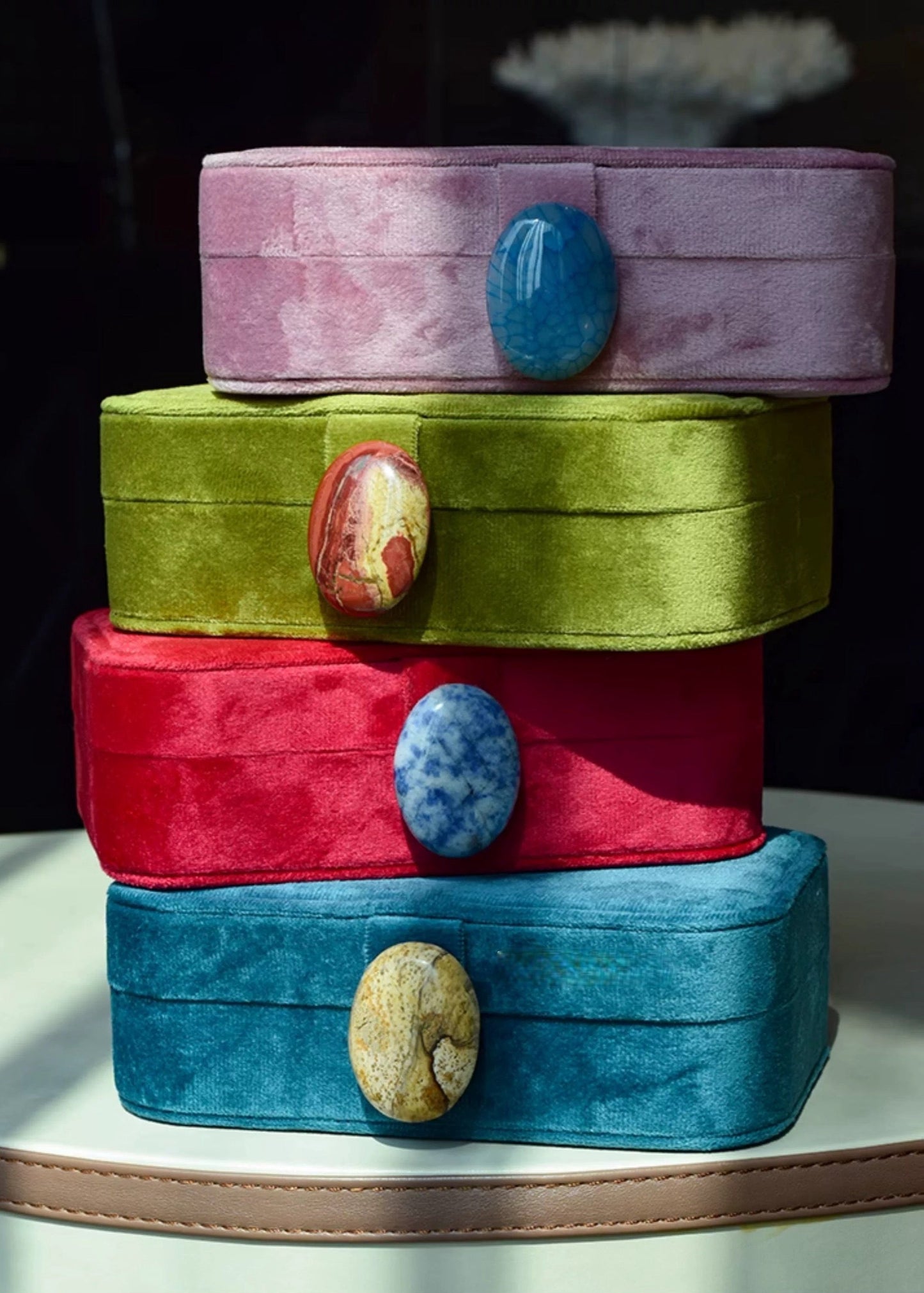 Stack of colorful velvet jewelry boxes with stone-like embellishments on a dark background