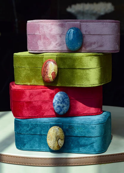 Stack of colorful velvet jewelry boxes with stone-like embellishments on a dark background