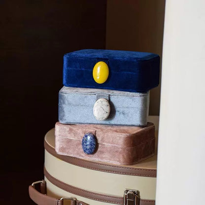 Stack of three velvet pearl jewelry boxes with embedded stones on a suitcase.