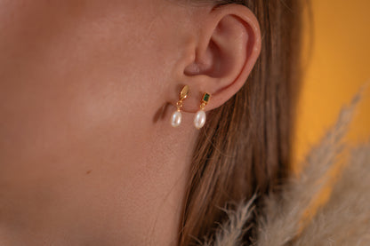 Close-up of an ear wearing gold and pearl earrings with a blurred background