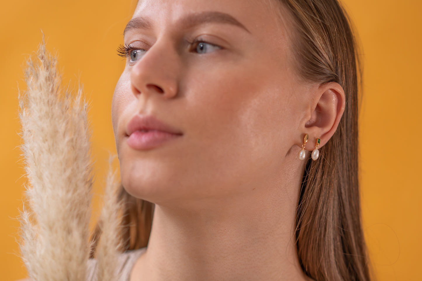 Woman wearing pearl earrings against a yellow background