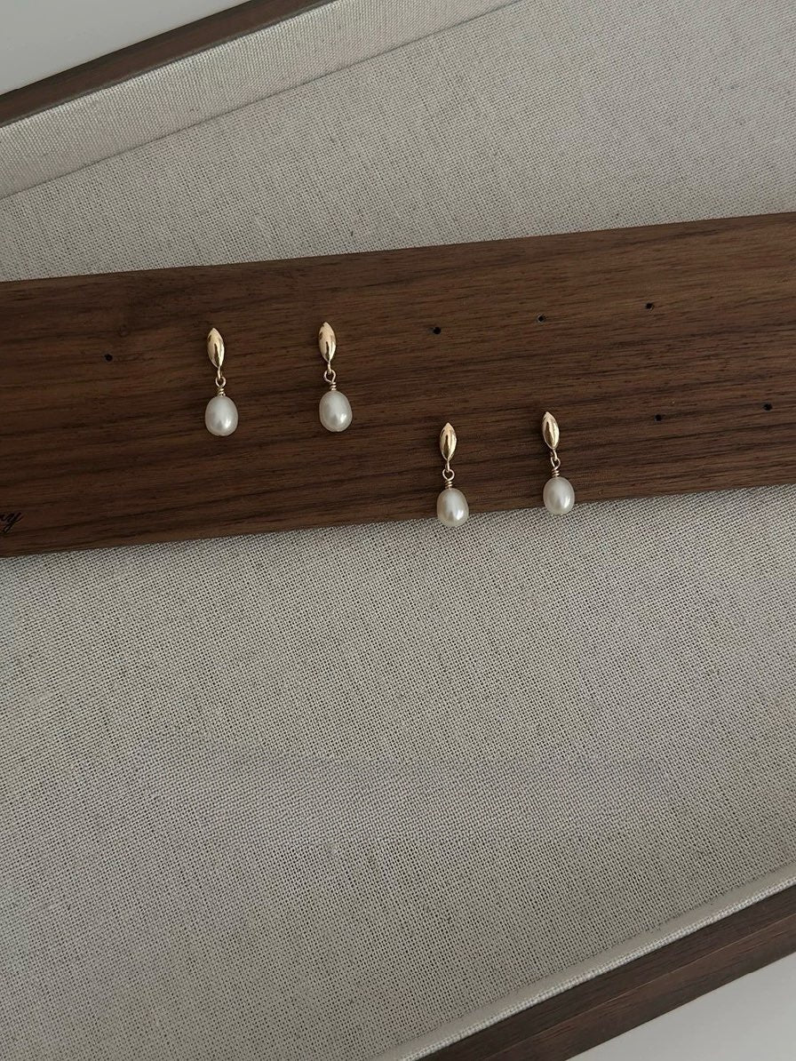 Set of pearl earrings displayed on a wooden rack against a neutral background