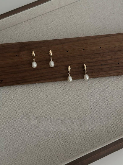 Set of pearl earrings displayed on a wooden rack against a neutral background