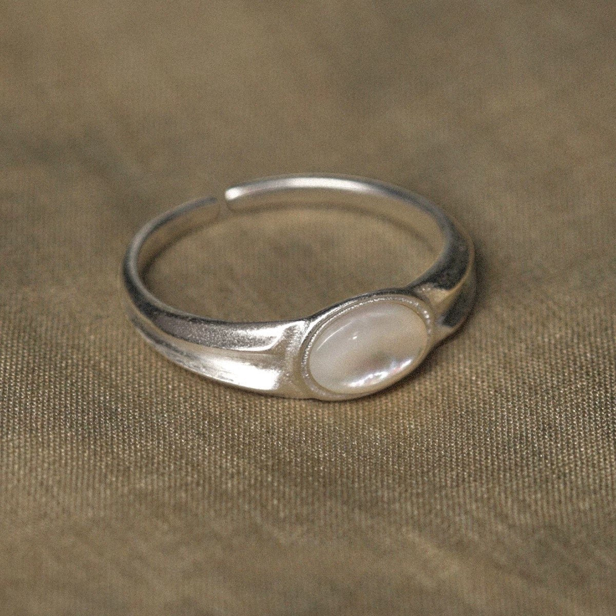Silver ring with a central nacre stone on a beige fabric background