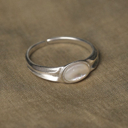 Silver ring with a central nacre stone on a beige fabric background