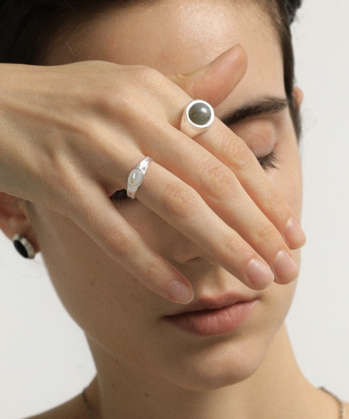 Close-up of a woman's face with rings on her fingers against a neutral background