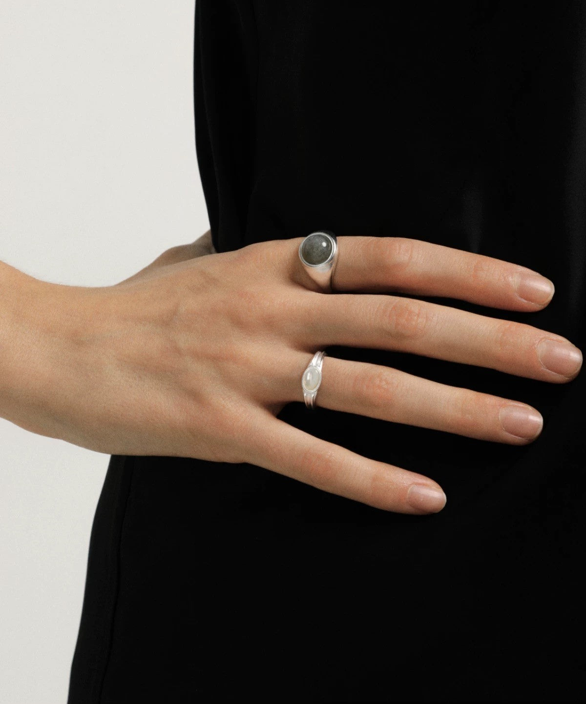 Hand wearing two silver rings on a plain background