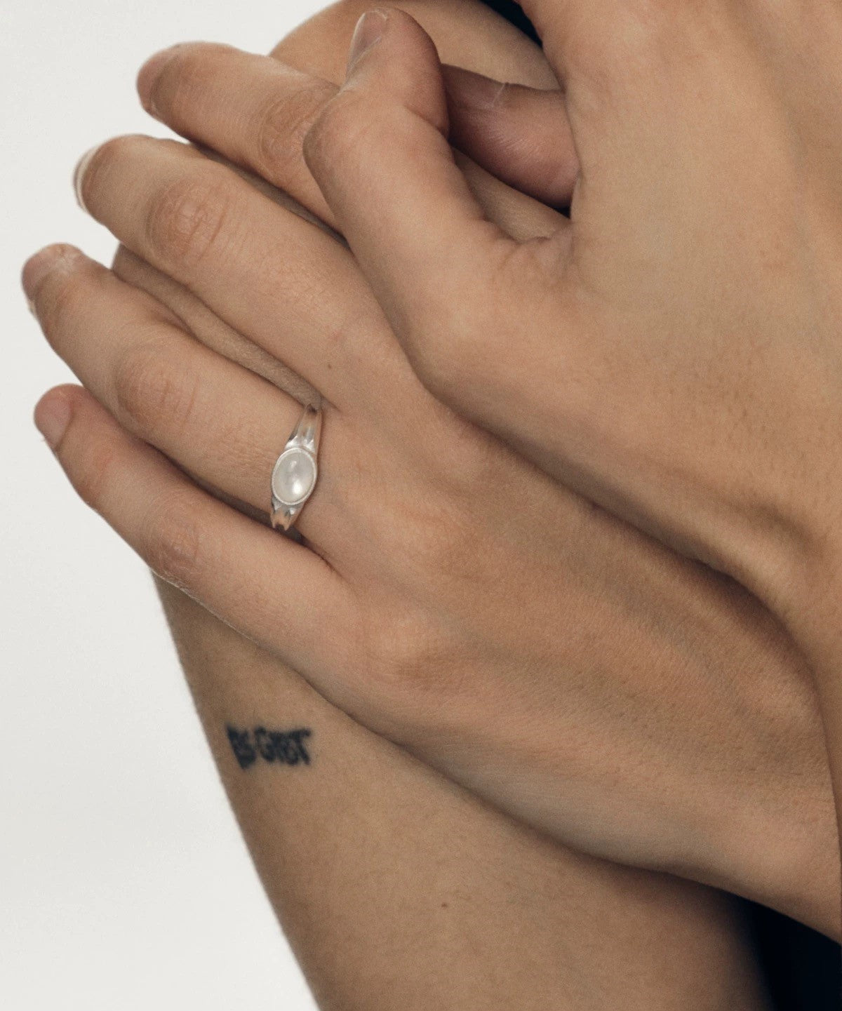 Close-up of a hand wearing a ring with a white nacre stone on a plain background