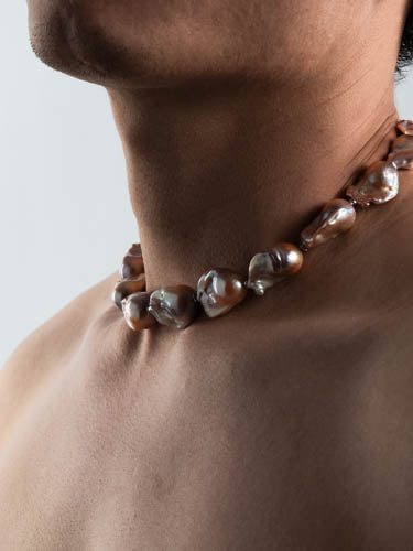 Baroque pearl necklace worn by a men a neutral background
