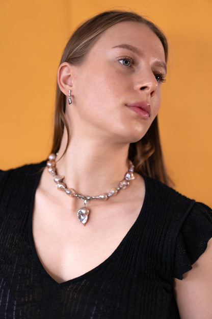 Woman wearing a purple pearl necklace with a pearl pendant against an orange background