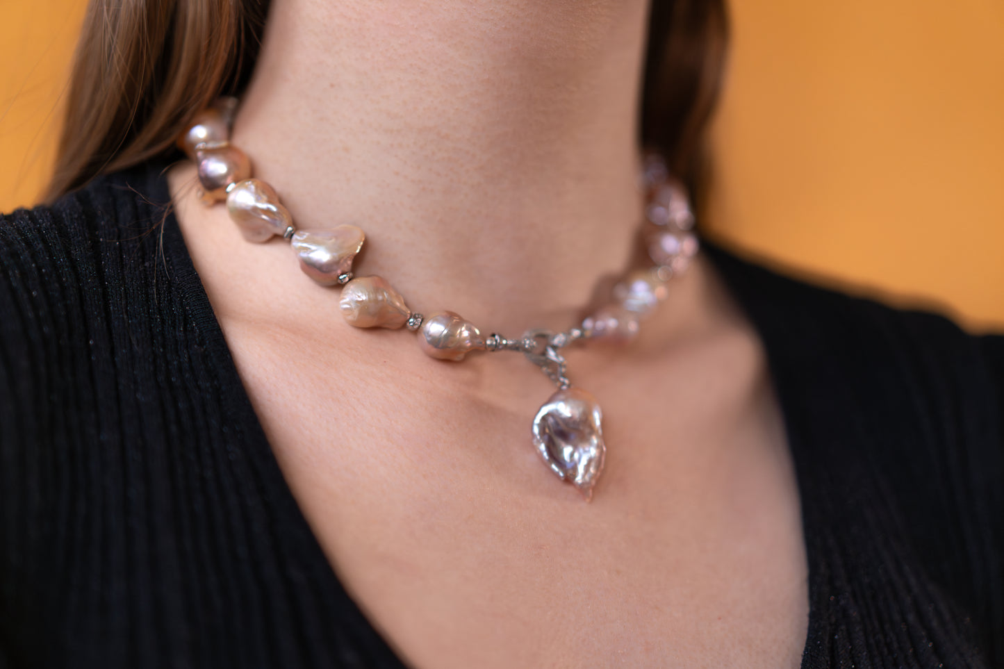 purple Pearl necklace with a silver pendant on a person wearing a black sweater.