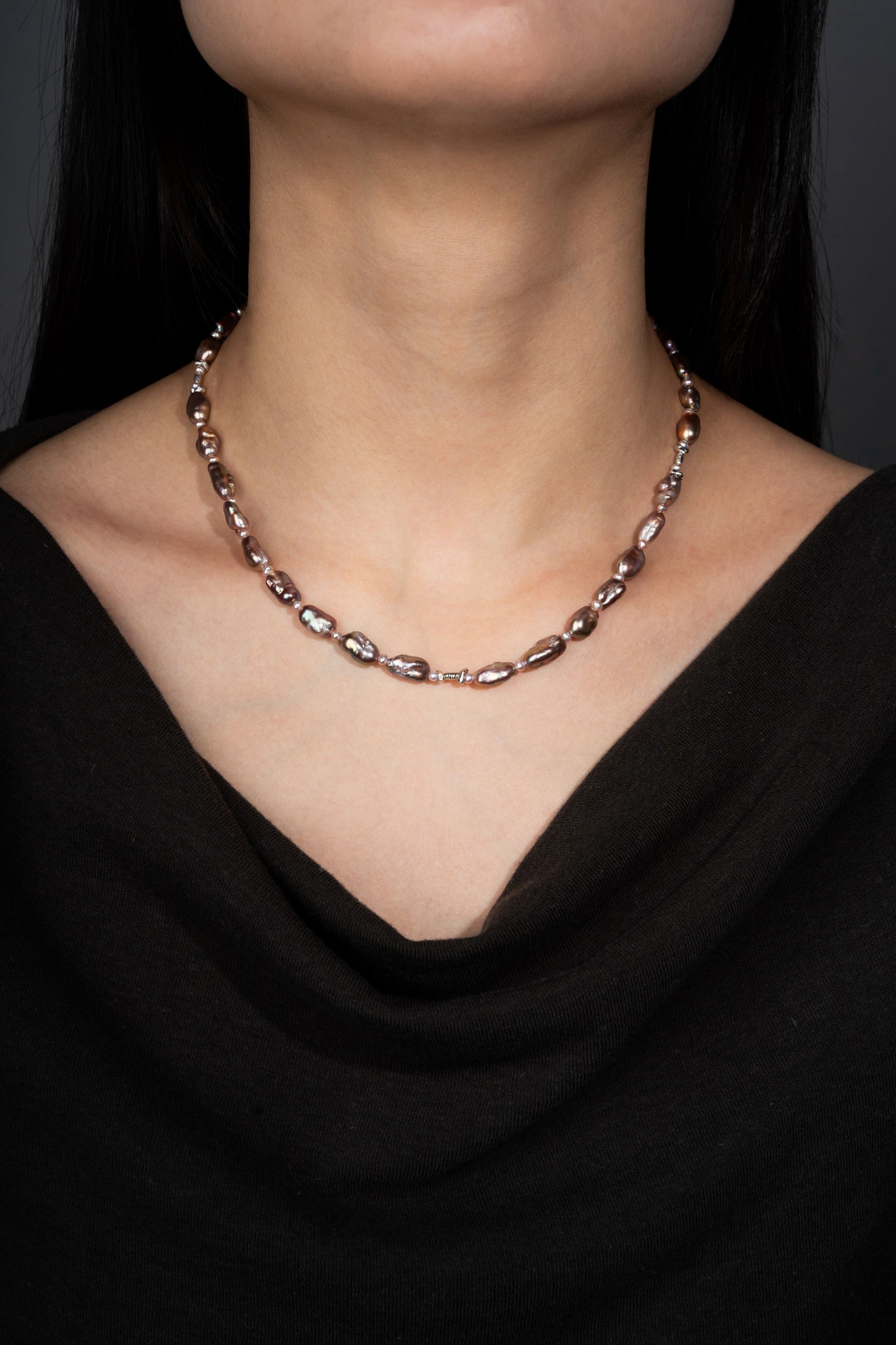 Keshi pearl necklace on a person wearing a black top against a dark background