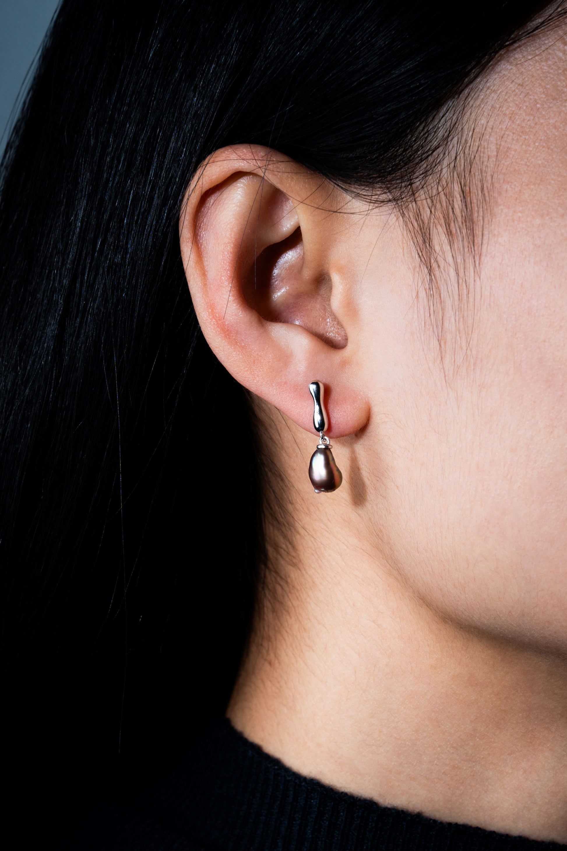 Close-up of an ear wearing a dangling Keshi pearl earring with a dark background