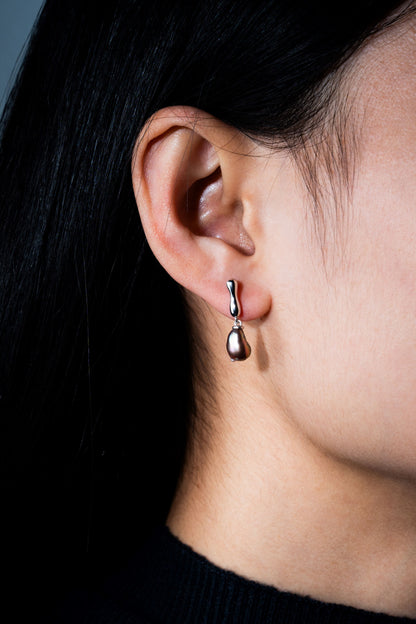 Close-up of an ear wearing a dangling Keshi pearl earring with a dark background