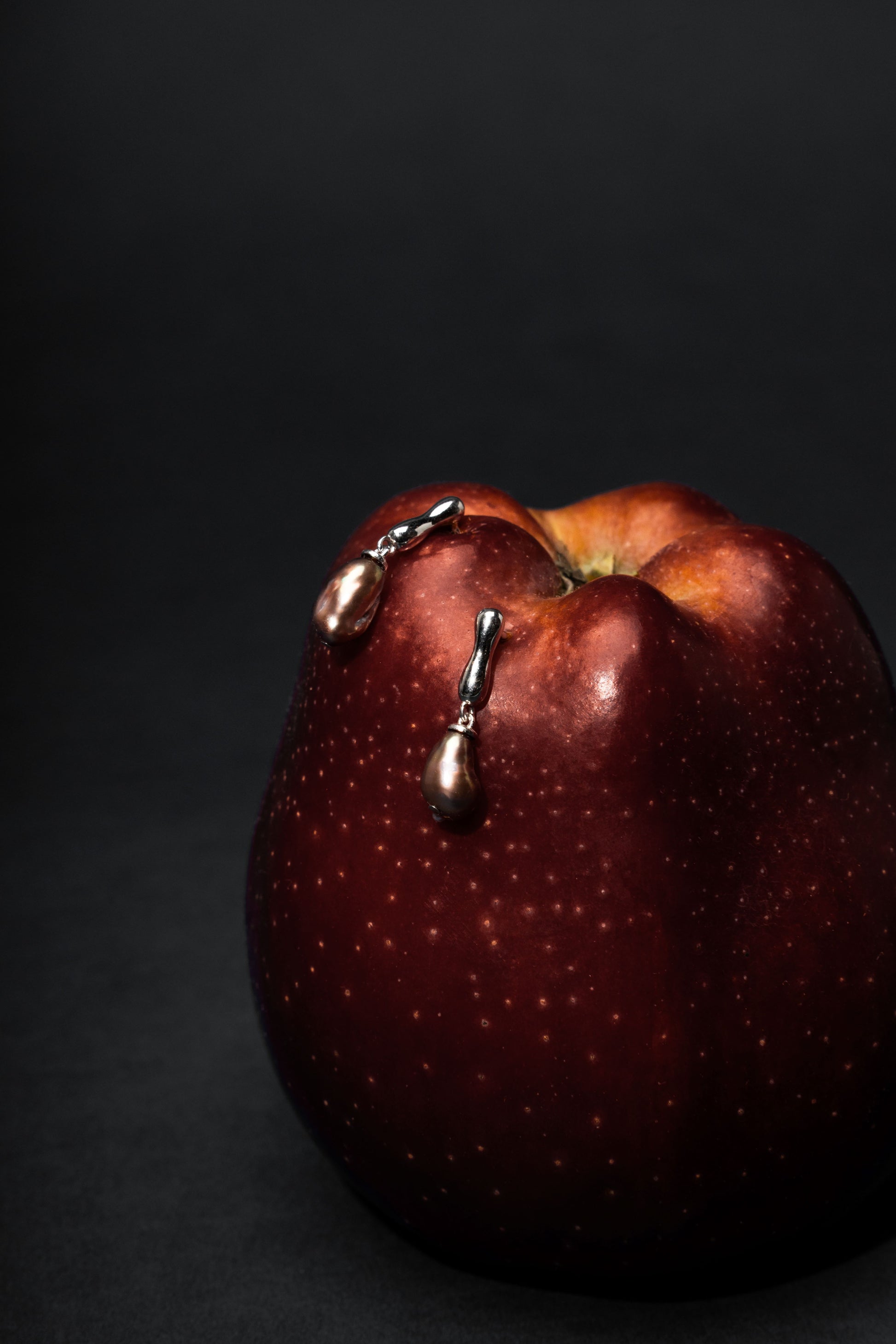 Red apple with Keshi pearl earrings on a black background