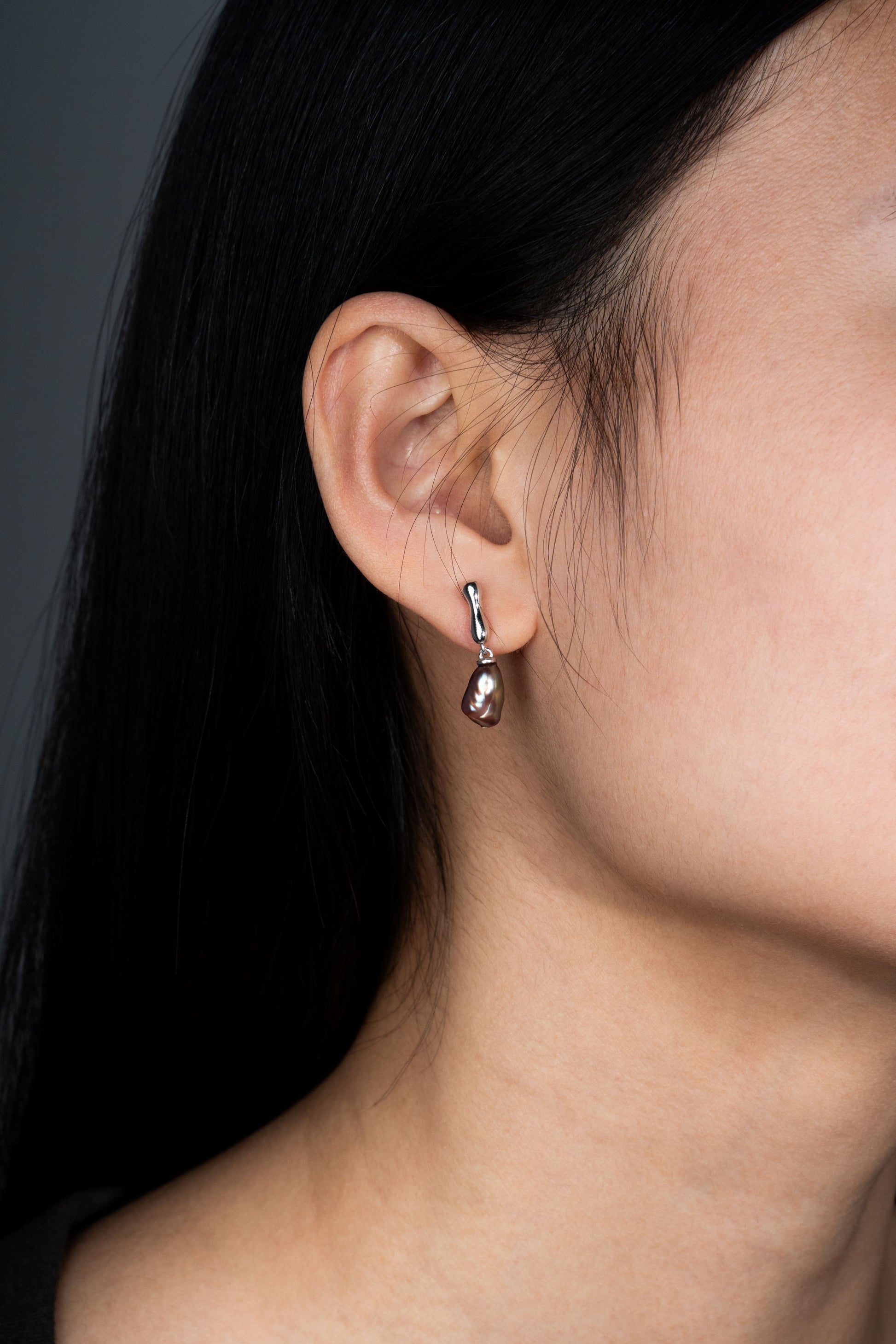Close-up of an ear wearing a dangling Keshi pearl earring with a dark background