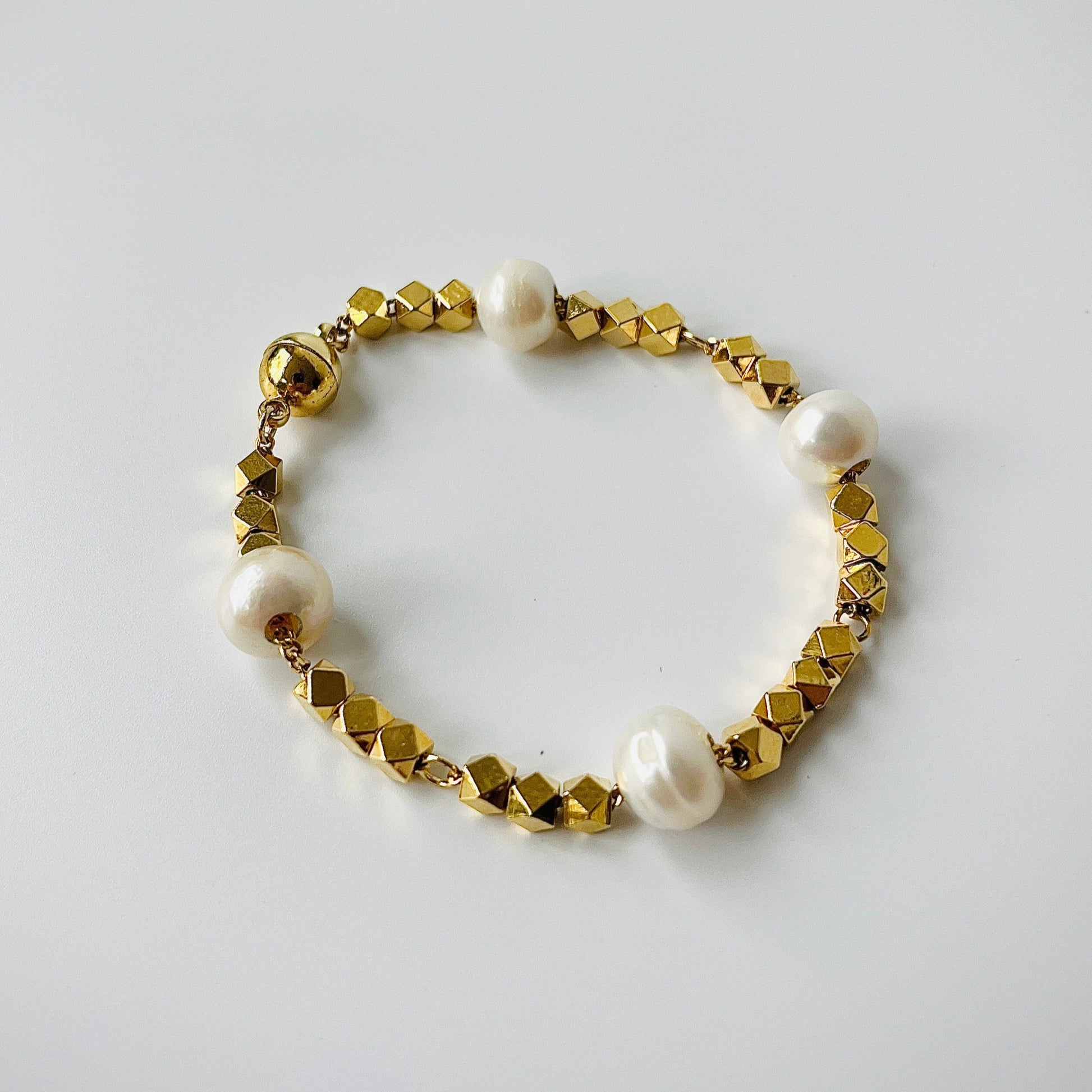 Bracelet with gold beads and freshwater pearls on a light gray background