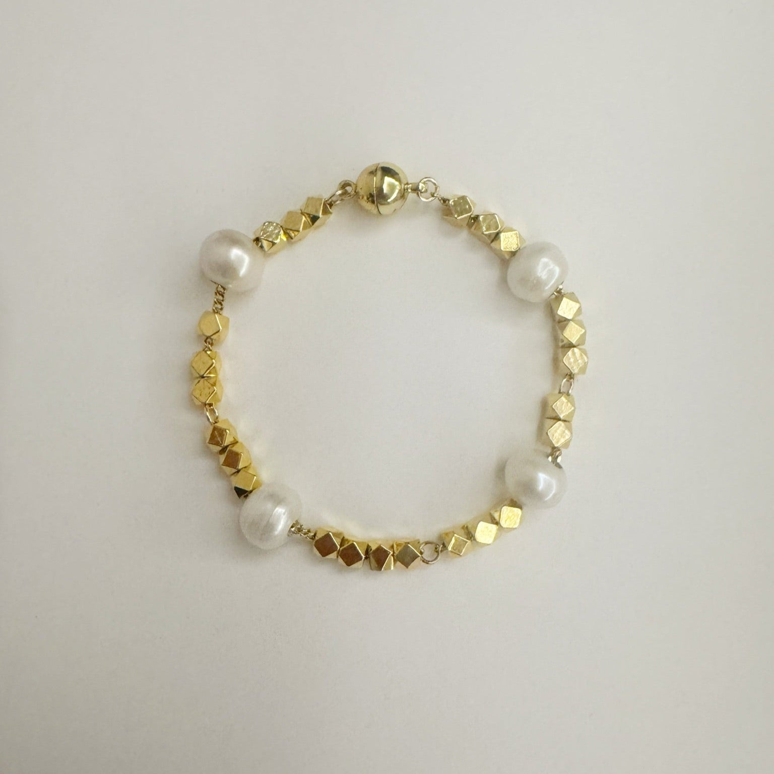 Bracelet with gold beads and freshwater pearls on a light gray background