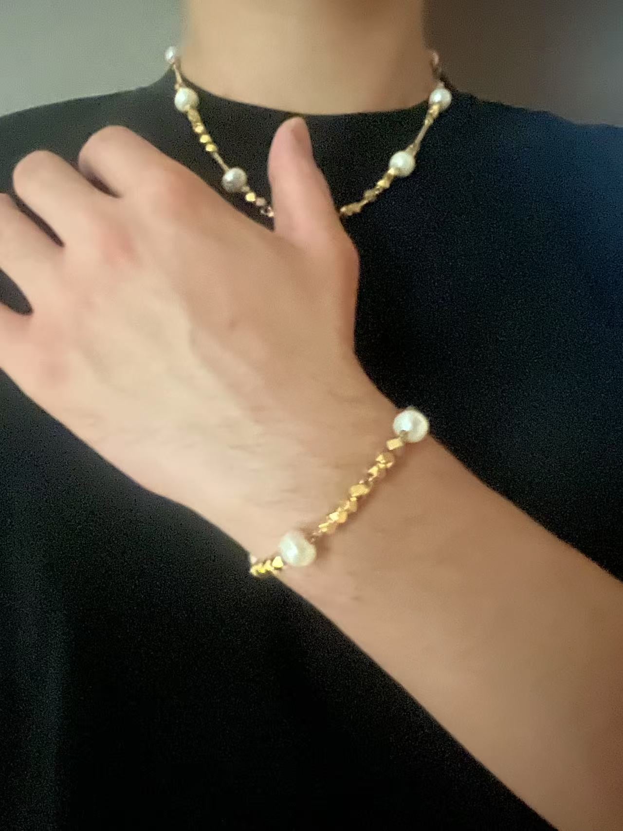 Gold pearl bracelet and necklace set against a black background
