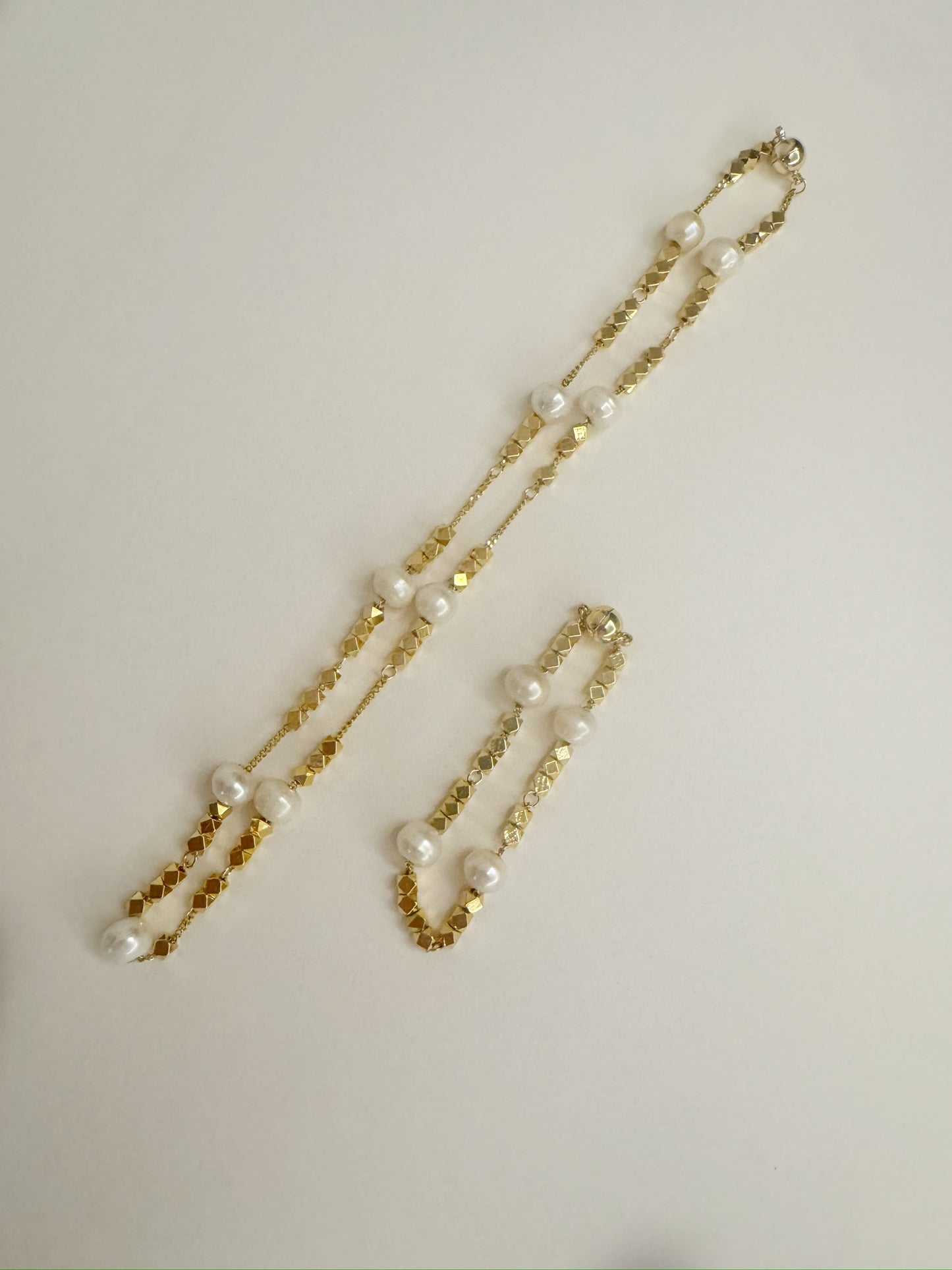 Gold necklace and bracelet set with white freshwater pearls on a light gray background