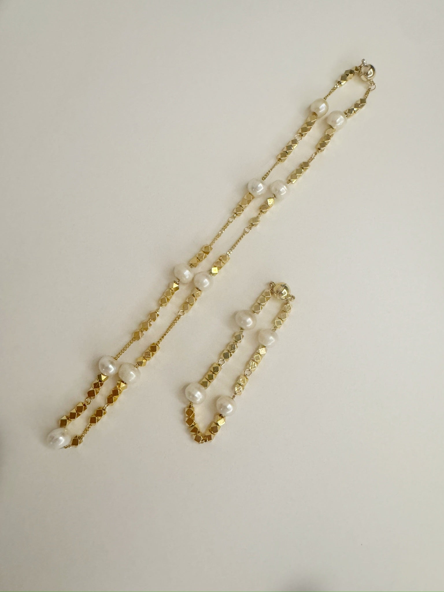 Gold necklace and bracelet set with white freshwater pearls on a light gray background