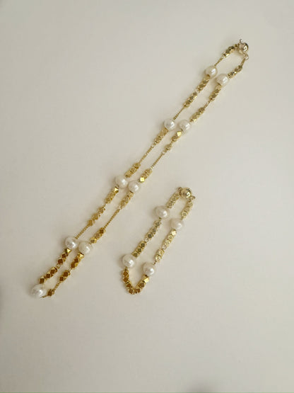 Gold necklace and bracelet set with white freshwater pearls on a light gray background
