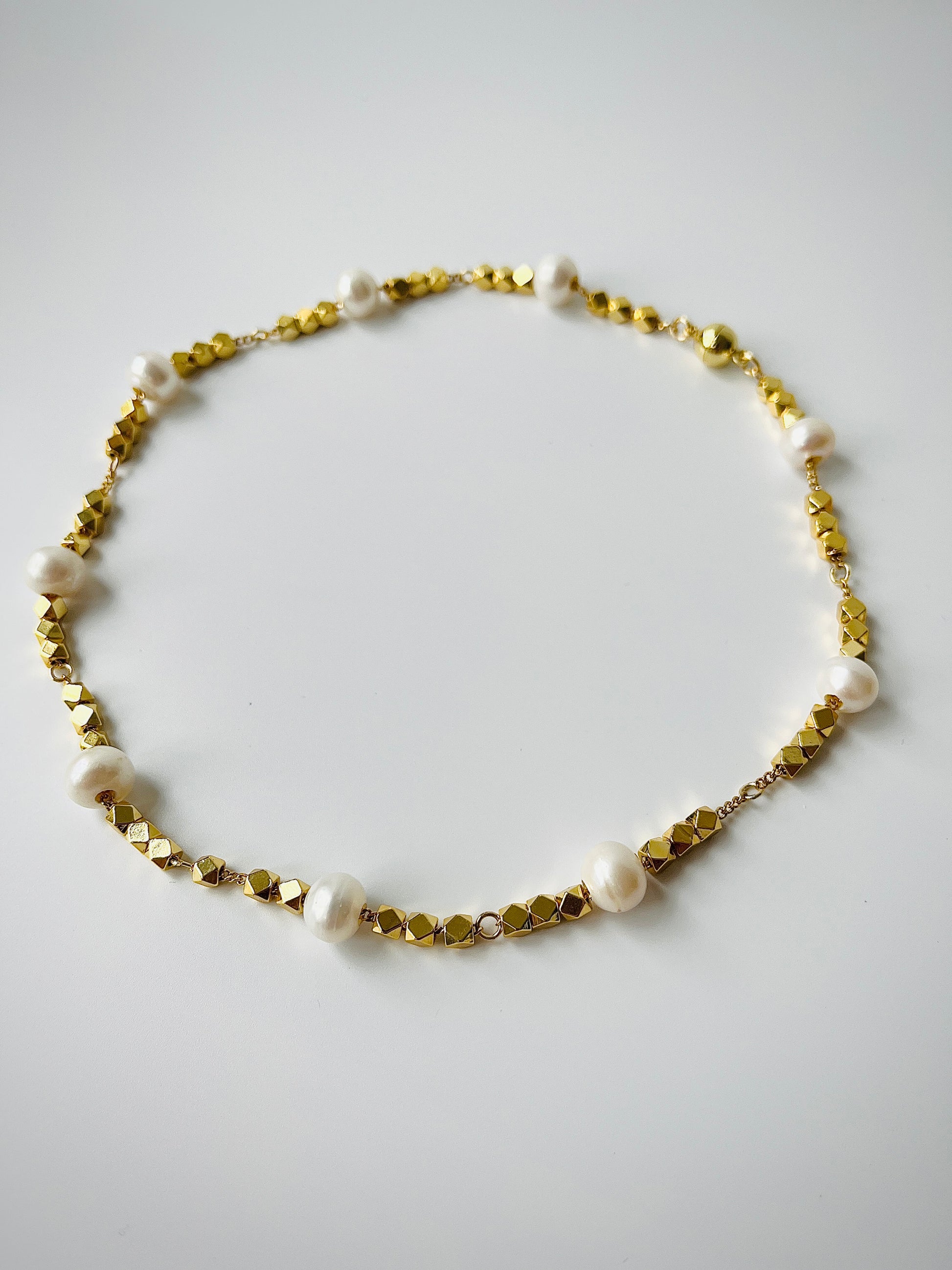 Necklace with gold beads and white freshwater pearls on a light gray background