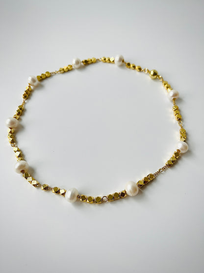 Necklace with gold beads and white freshwater pearls on a light gray background