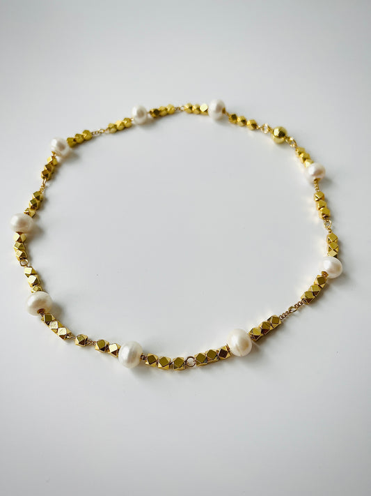 Necklace with gold beads and white freshwater pearls on a light gray background