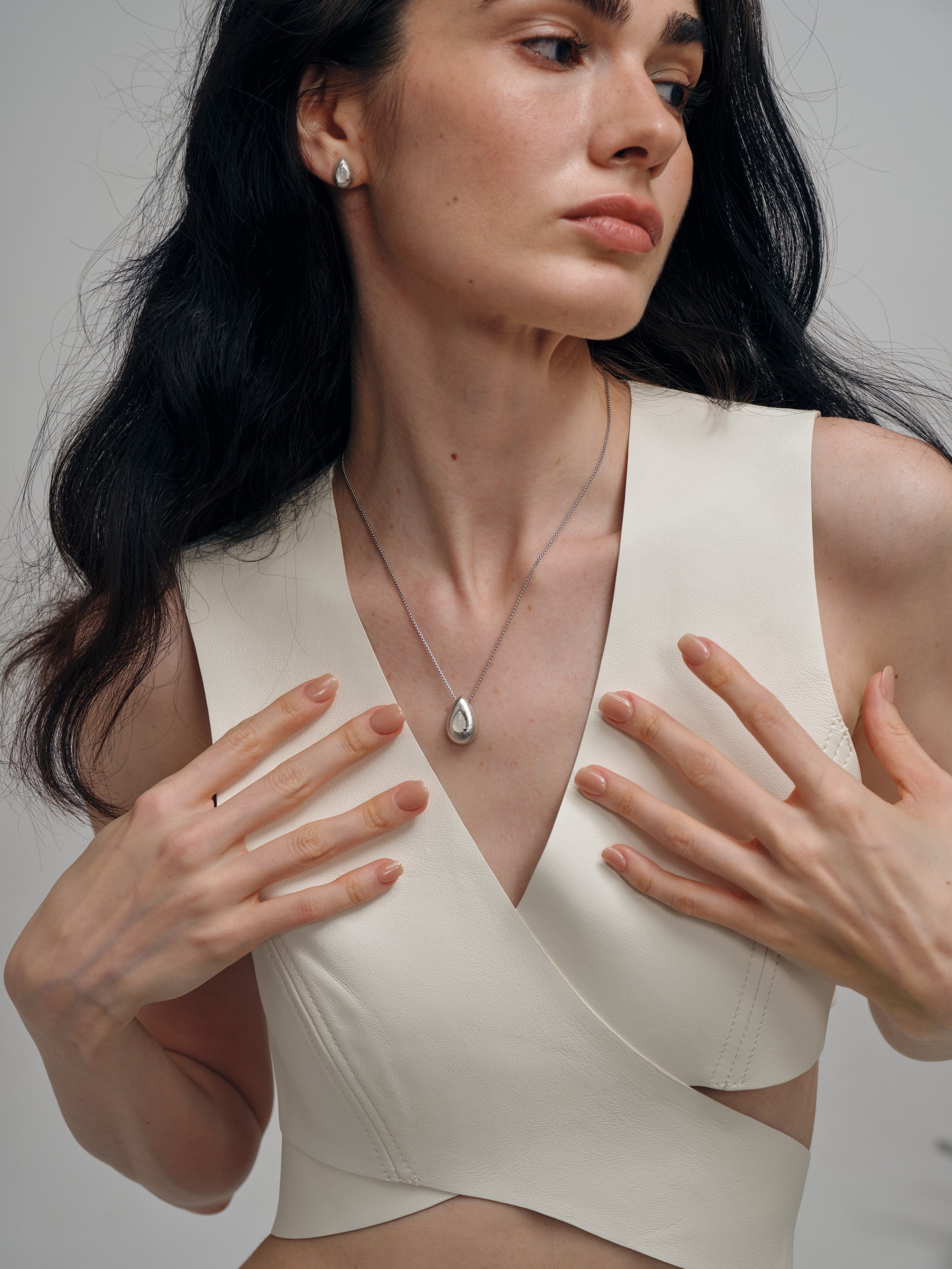 Woman wearing a white sleeveless top with a necklace with a white agate gemstone against a neutral background