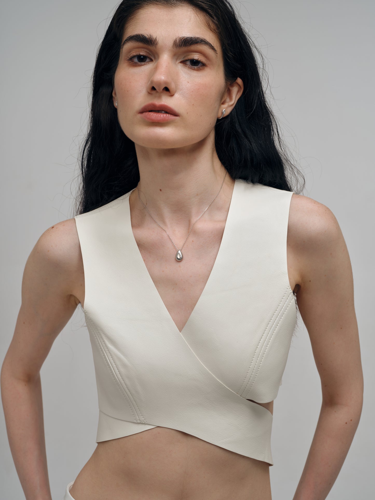 Woman wearing a beige sleeveless top with a white agate necklace against a plain background