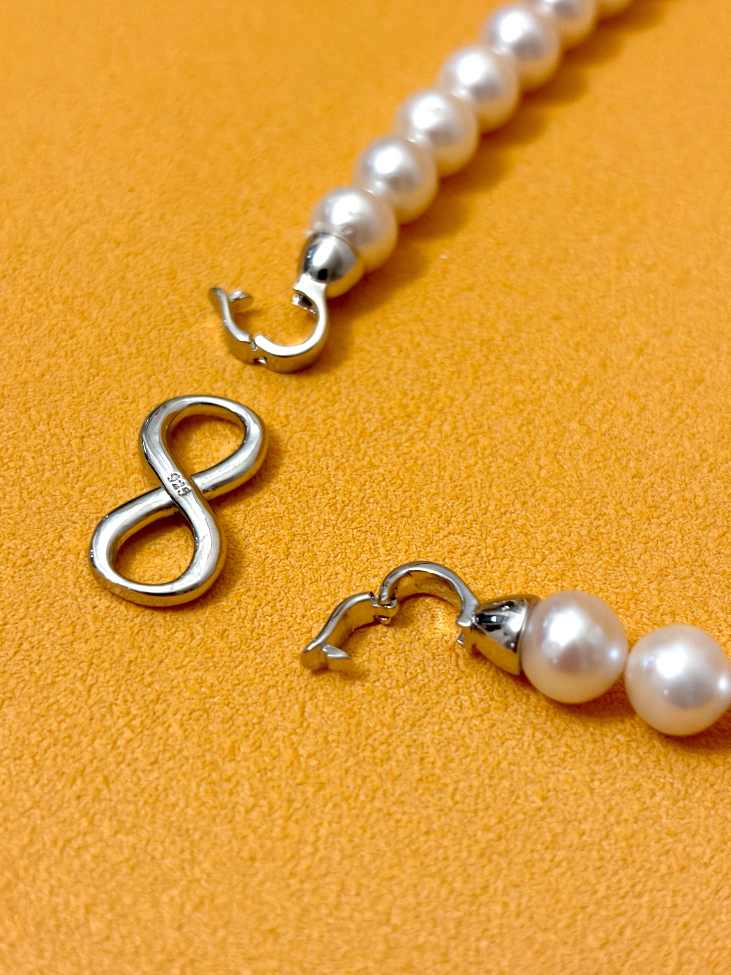 Pearl necklace with silver clasp on a mustard yellow background