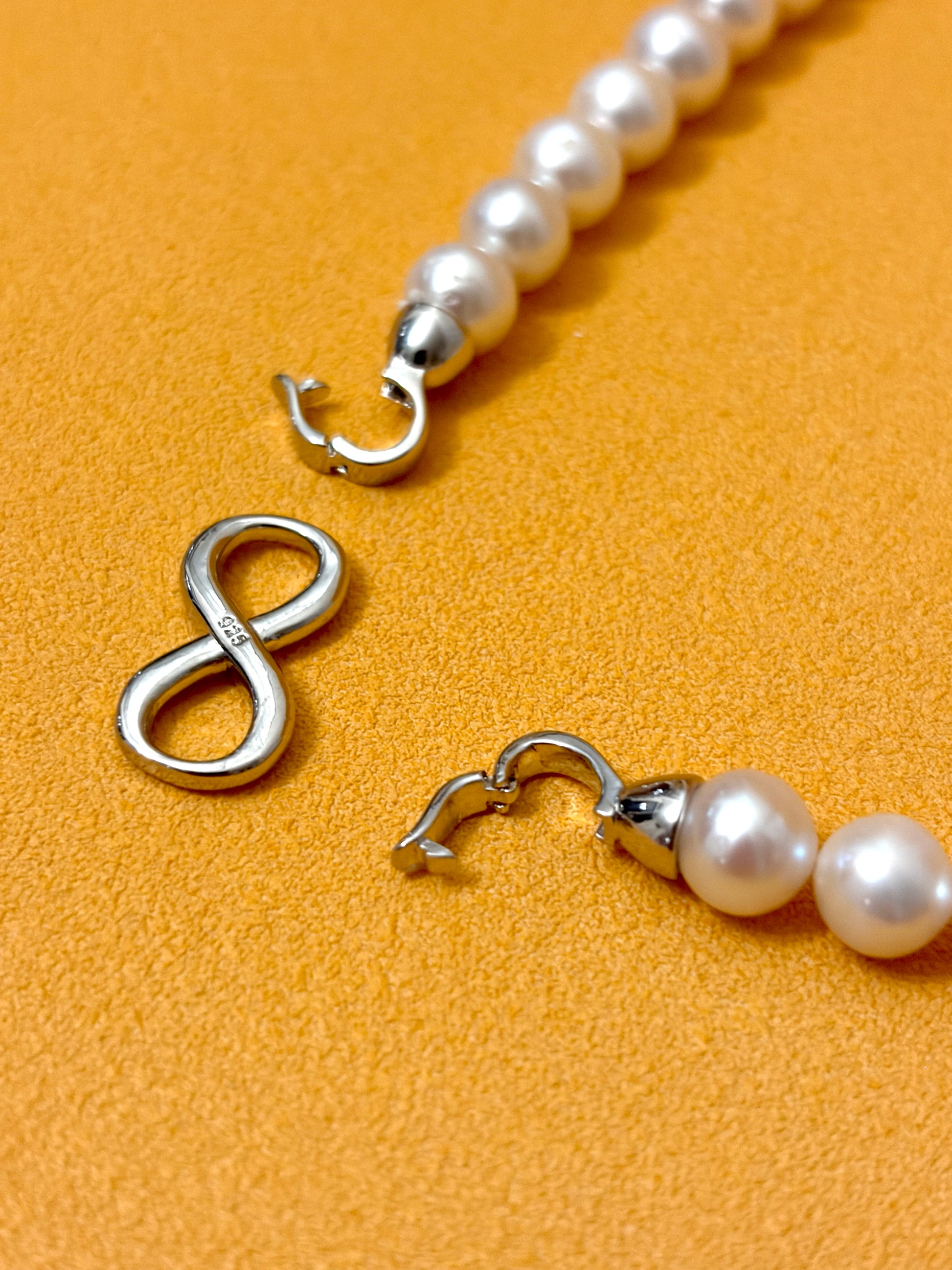Pearl necklace with silver clasp on a mustard yellow background