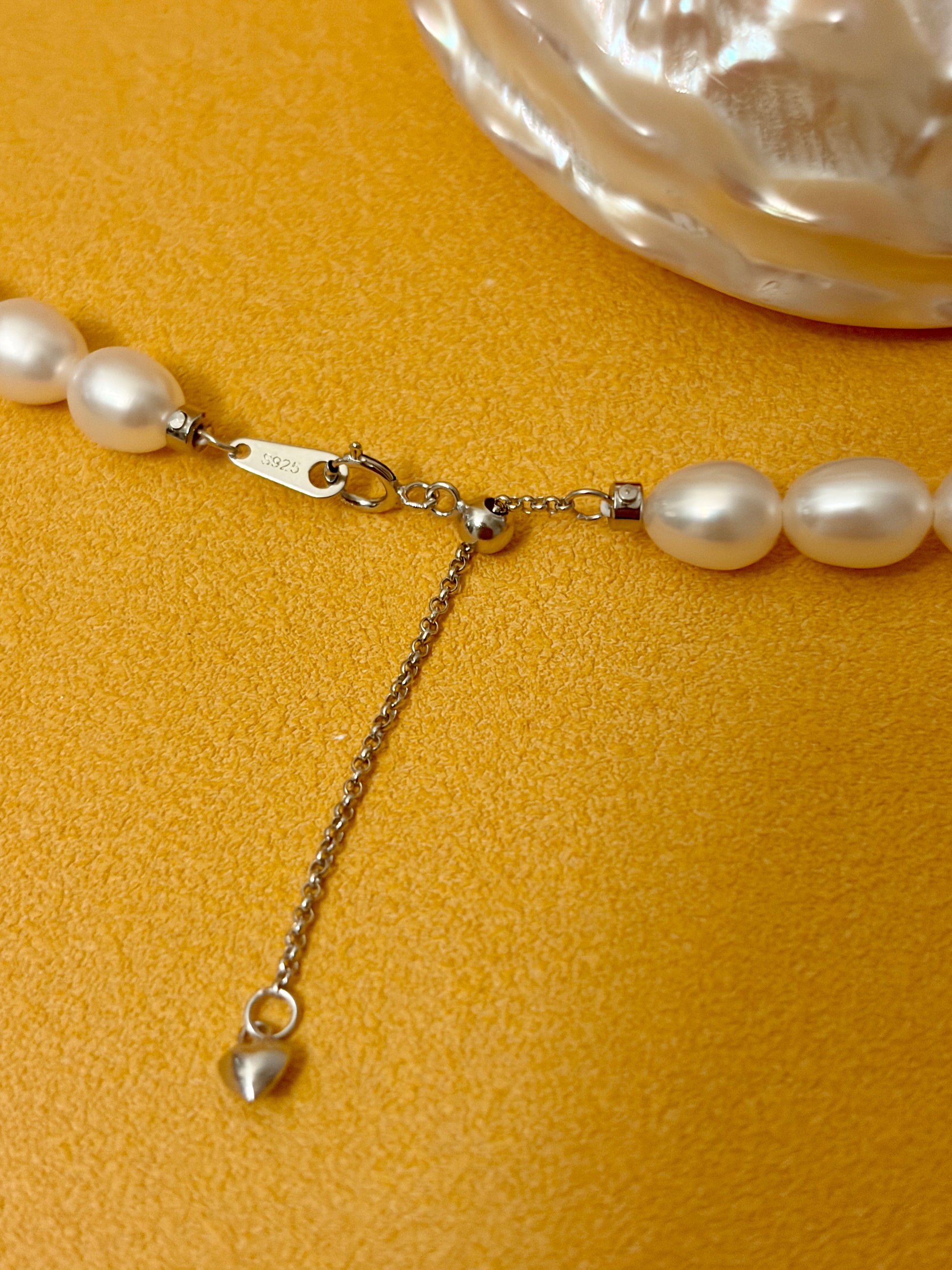 Pearl necklace with a heart charm on a yellow background