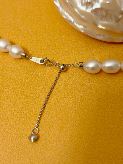 Pearl necklace with a heart charm on a yellow background