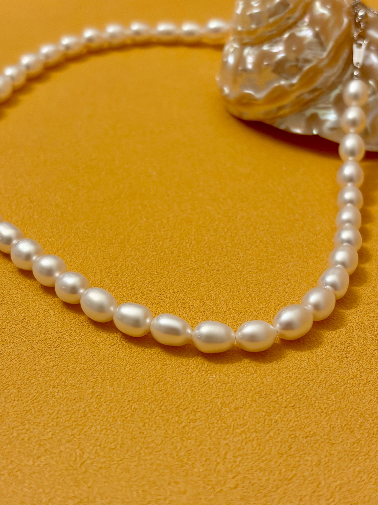 Pearl necklace on a textured yellow surface with a shell in the background