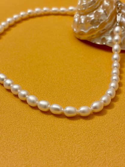 Pearl necklace on a textured yellow surface with a shell in the background